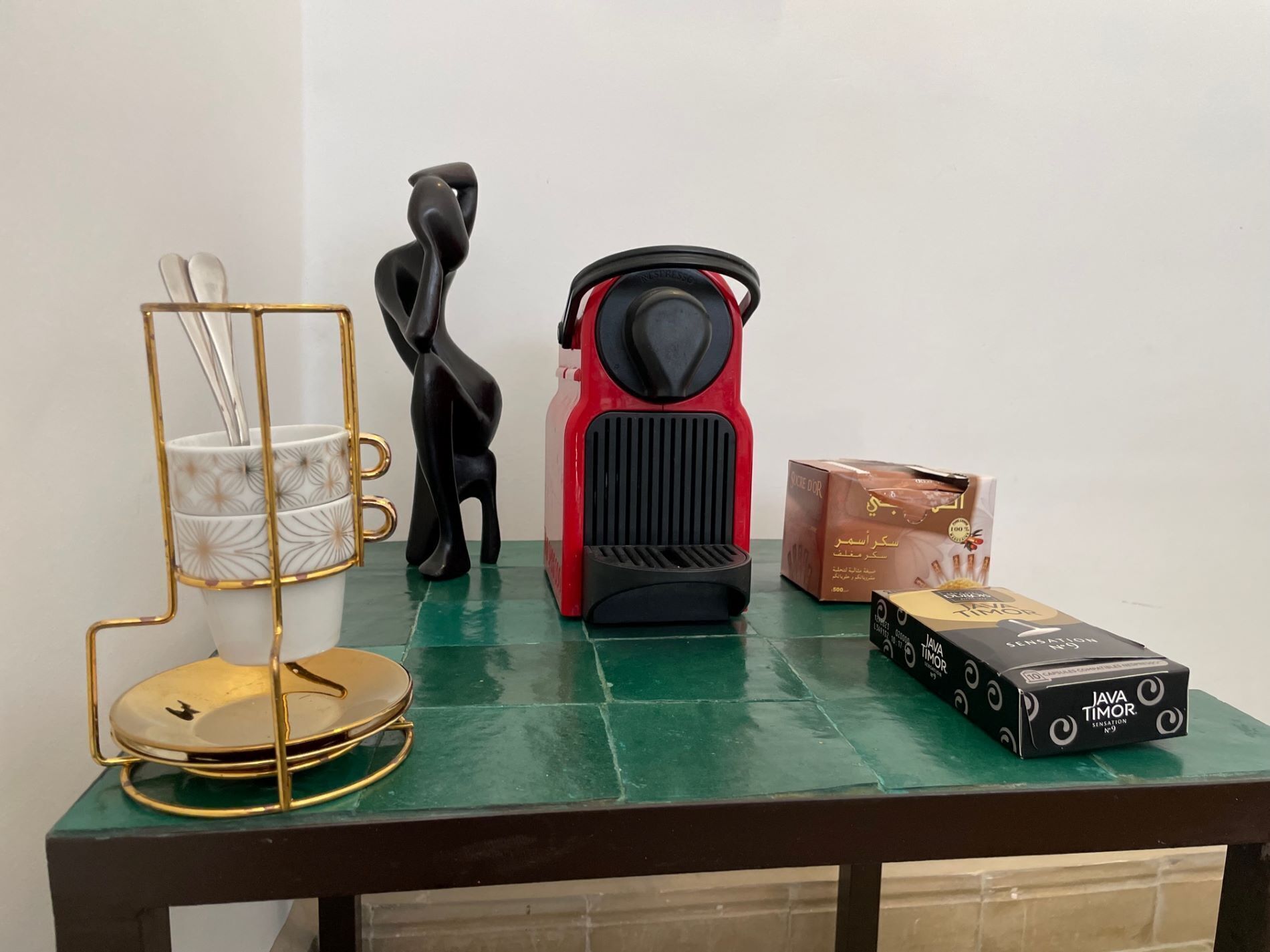 Ein Tisch mit einer Kaffeemaschine, einer schwarzen Dekorationsskulptur, einem Kaffeebecherhalter und einer Packung Java Timor Zigaretten.