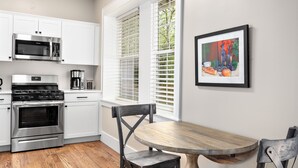 A kitchen with white cabinets, stainless steel appliances, a wooden dining table, and a framed artwork on the wall.