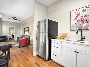 A modern kitchen with a stainless steel refrigerator, white cabinetry, and a wooden floor.