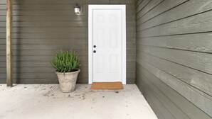 A white door with a small potted plant beside it, a doormat, and a wall with horizontal siding.