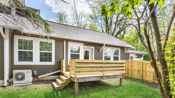 A house with a wooden deck, a staircase leading to a door, and a fenced yard.