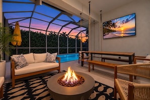 A modern outdoor living space with a fire pit, seating, and a view of a swimming pool at sunset. - ☀ Bike to Ritz & Beaches, 3 Kings, 2 Masters, Easy, Bikes, Heated Pool ☀ (Naples)