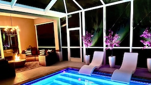 A swimming pool with lounge chairs and a fire pit, surrounded by large windows and potted plants. - ☀ Bike to Ritz & Beaches, 3 Kings, 2 Masters, Easy, Bikes, Heated Pool ☀ (Naples)