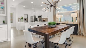 A modern kitchen with white cabinetry, a central island, and a dining area with a wooden table and white chairs. - ☀ Bike to Ritz & Beaches, 3 Kings, 2 Masters, Easy, Bikes, Heated Pool ☀ (Naples)