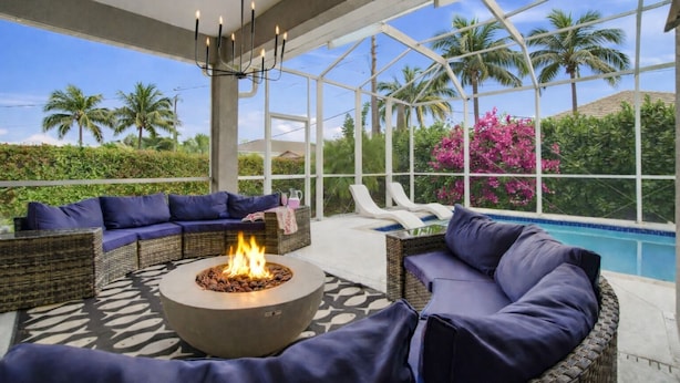 An outdoor lounge area with a fire pit, seating, and a view of a swimming pool and palm trees. - ☀ Bike to Ritz & Beaches, 3 Kings, 2 Masters, Easy, Bikes, Heated Pool ☀ (Naples)