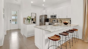 A modern kitchen with white cabinetry, a granite countertop, stainless steel appliances, and a central island with stools. - ☀ Bike to Ritz & Beaches, 3 Kings, 2 Masters, Easy, Bikes, Heated Pool ☀ (Naples)