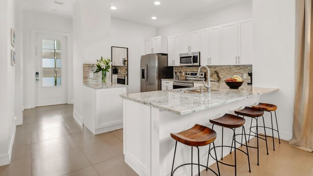 A modern kitchen with white cabinetry, a granite countertop, stainless steel appliances, and a central island with stools. - ☀ Bike to Ritz & Beaches, 3 Kings, 2 Masters, Easy, Bikes, Heated Pool ☀ (Naples)