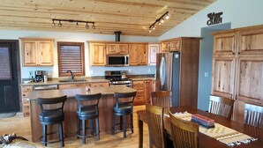 Une cuisine moderne avec des meubles en bois, un îlot central doté de tabourets, un four à micro-ondes, une cuisinière et un réfrigérateur.