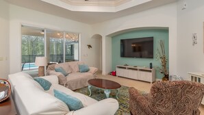 A spacious living room with a ceiling fan, a large TV, and a pool visible through the glass doors. - 4 BR House w/ heat-pump pool! (Dunnellon)