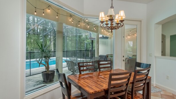 A dining area with a wooden table and chairs, a chandelier, and a view of a swimming pool through large windows. - 4 BR House w/ heat-pump pool! (Dunnellon)