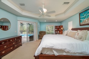 A bedroom with a large bed, a ceiling fan, a wooden dresser, and a bookshelf.
