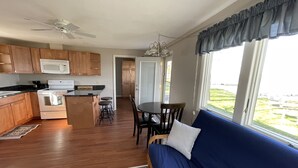 A modern kitchen with wooden cabinets, a white microwave, and a stove. There is a dining area with a blue sofa and a table.