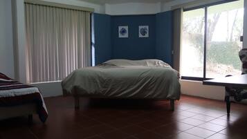 A bedroom with a bed, a chair, a window with blinds, and two wall-mounted pictures.