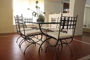 A dining area with a table and four chairs, a potted plant, and a window with blinds.