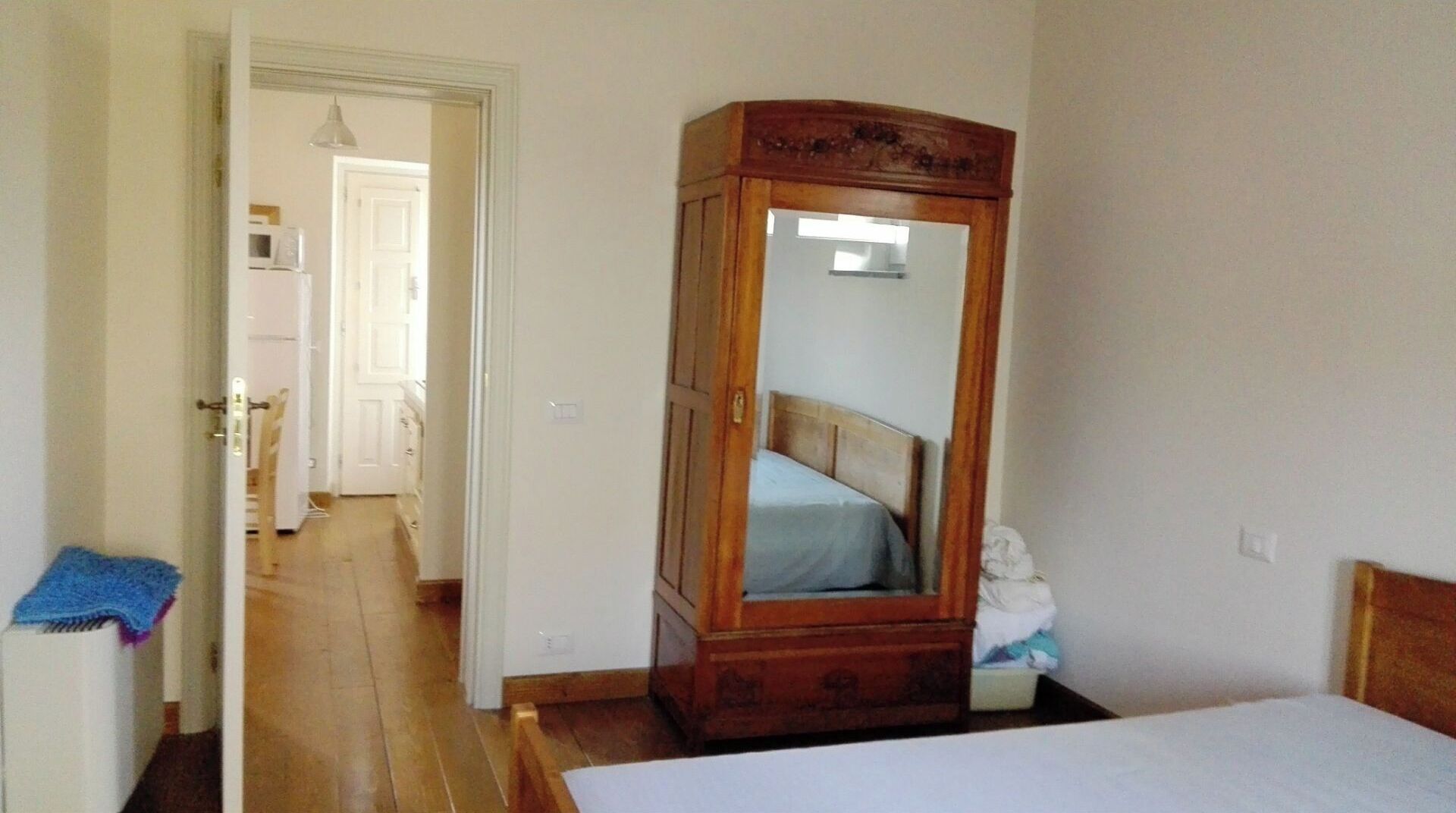 Ein Schlafzimmer mit einem Holfischschrank, einem Bett und einem Spiegel, der den Raum widerspiegelt.