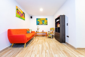 A living room with a bright orange sofa, a wooden coffee table, a colorful armchair, and a bookshelf. - Hotel Le Biciclette (Guarne)