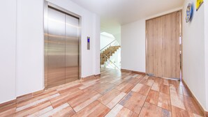 Un pasillo moderno con suelo de madera, un ascensor y una escalera que sube a otro piso.