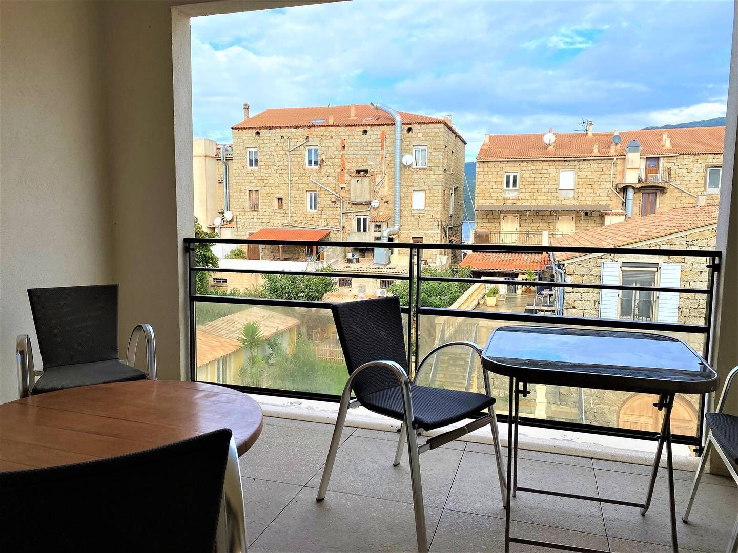 Een balkon met een tafel en stoelen, met uitzicht op een stadsgezicht met stenen gebouwen.