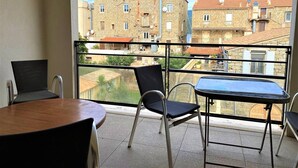En balkon med et bord og stole, der udover en byudsigt med bygninger i sten.