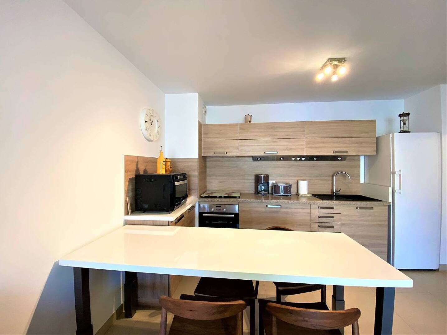 Een moderne keuken met houten kastjes, een wit aanrecht, een inbouwoven en een koelkast.