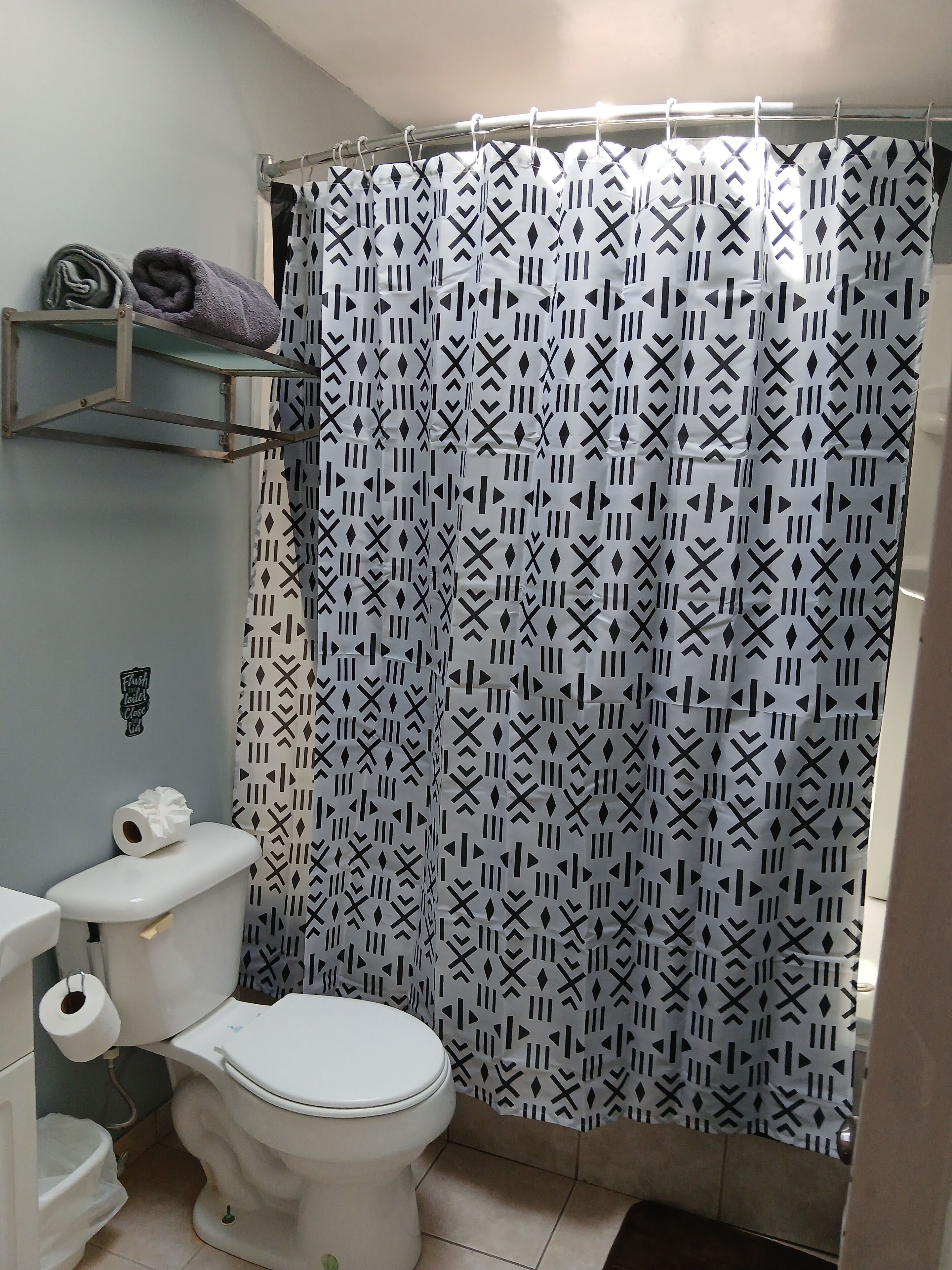Un baño con inodoro, cortina de ducha con diseño geométrico y estante con toallas.
