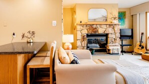A cozy living room with a stone fireplace, a television, and a guitar.