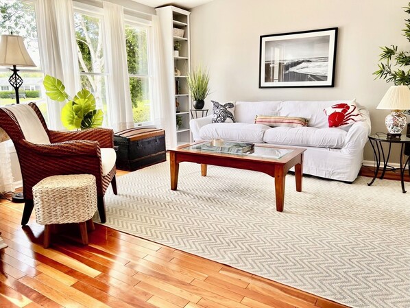 A living room with a white sofa, a wooden coffee table, a wicker chair, and a bookshelf.