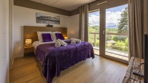 Quarto com uma cama grande, uma mesinha de cabeceira, uma janela com vista para áreas verdes e uma cabeceira de madeira.