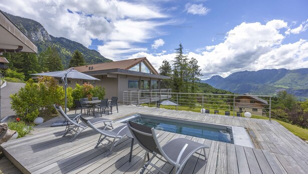 Um deck de madeira com piscina, espreguiçadeiras e área de refeições com vista para uma paisagem montanhosa.