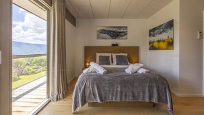 Quarto com uma cama grande, vista de uma paisagem montanhosa pela janela e duas pinturas na parede.