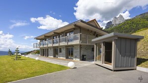 Una casa moderna a due piani con ampie finestre, un balcone e vista sulle montagne.