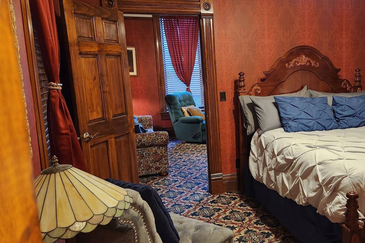 A bedroom with a bed, a chair, a lamp, and a door.