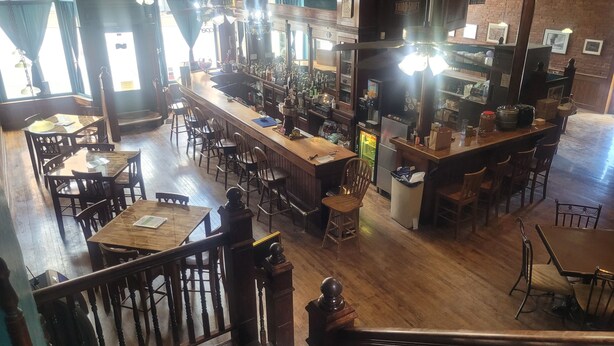 A bar area with wooden tables and chairs, a counter with various bottles, and a staircase leading to another level. - The Stampmill Victorian Suites (Lead)