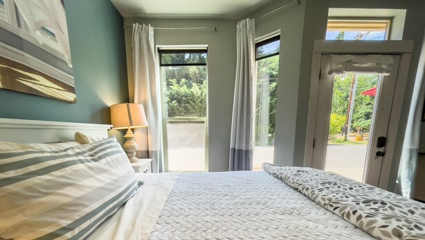A bedroom with a bed, a nightstand, a lamp, and a view of the outdoors through a door. - Jacksonville Towne Square.  (Jacksonville)