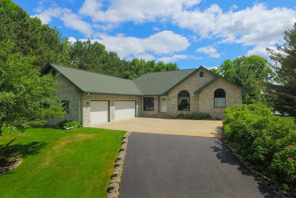 A two-story house with a stone facade, a green roof, and a driveway leading to a garage.