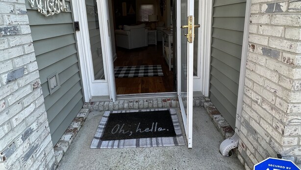 Une entrée de maison avec une pancarte « Bienvenue », un paillasson et un panneau d’avertissement de sécurité.