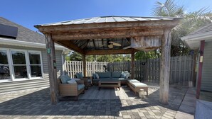 Un patio couvert aménagé avec des meubles en osier et un ventilateur de plafond.