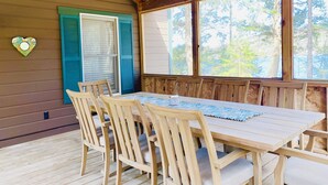 Um deck de madeira com mesa e cadeiras, uma decoração em formato de coração e uma janela com vista para árvores.