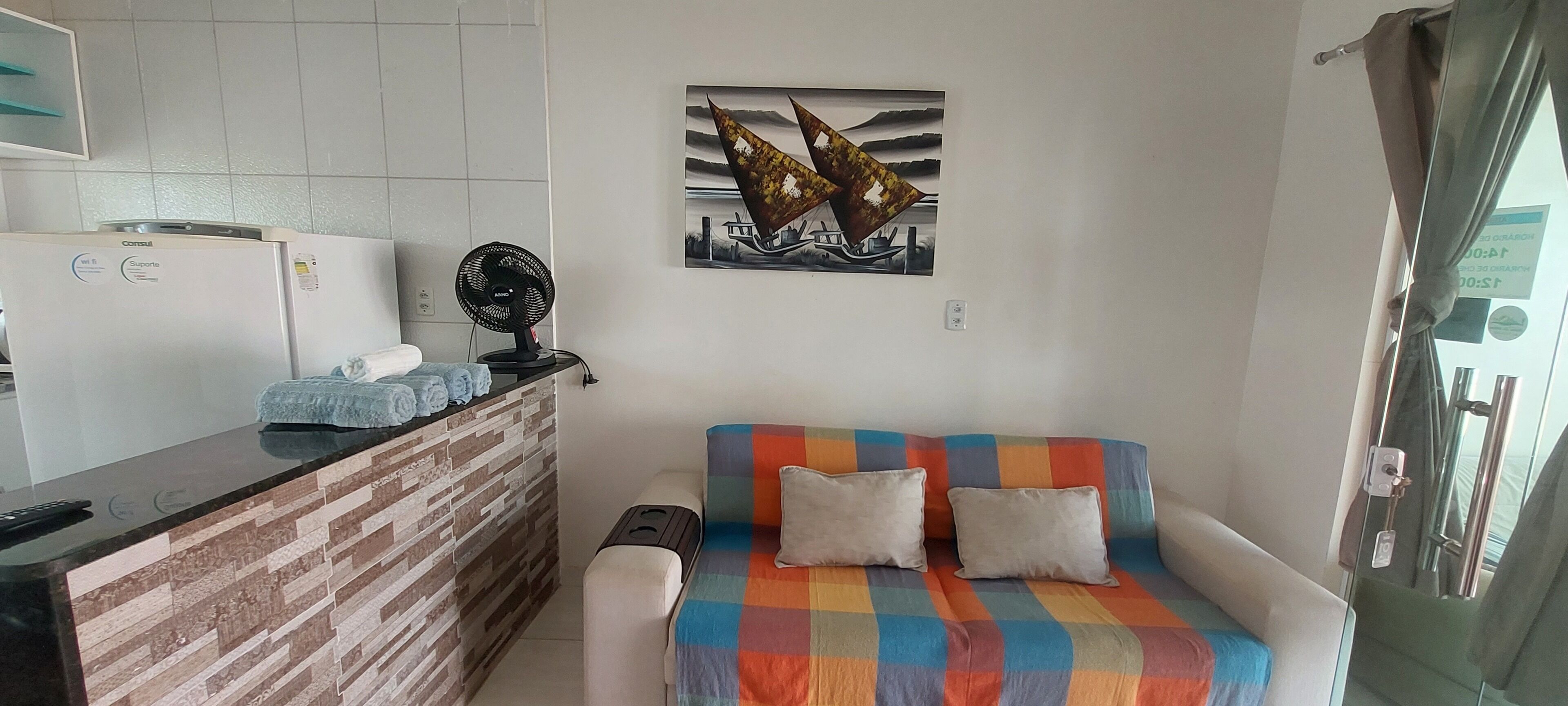 A compact living space with a kitchenette, a sofa with a colorful blanket, and a wall-mounted artwork.