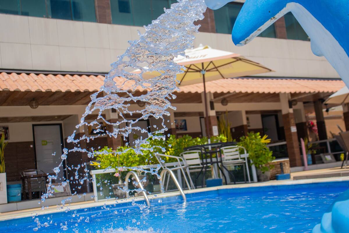 A swimming pool with water splashing, surrounded by outdoor seating and a building with a tiled roof.