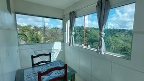 Ein Balkon mit Blick auf einen bewaldeten Hang, ein Stuhl und ein Tisch mit gemustertem Tuch.