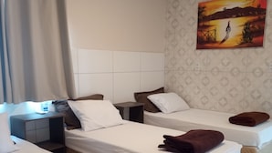 Ein Hotelzimmer mit drei Betten, einem Kopfteil, einem Bild an der Wand und einem Vorhang.