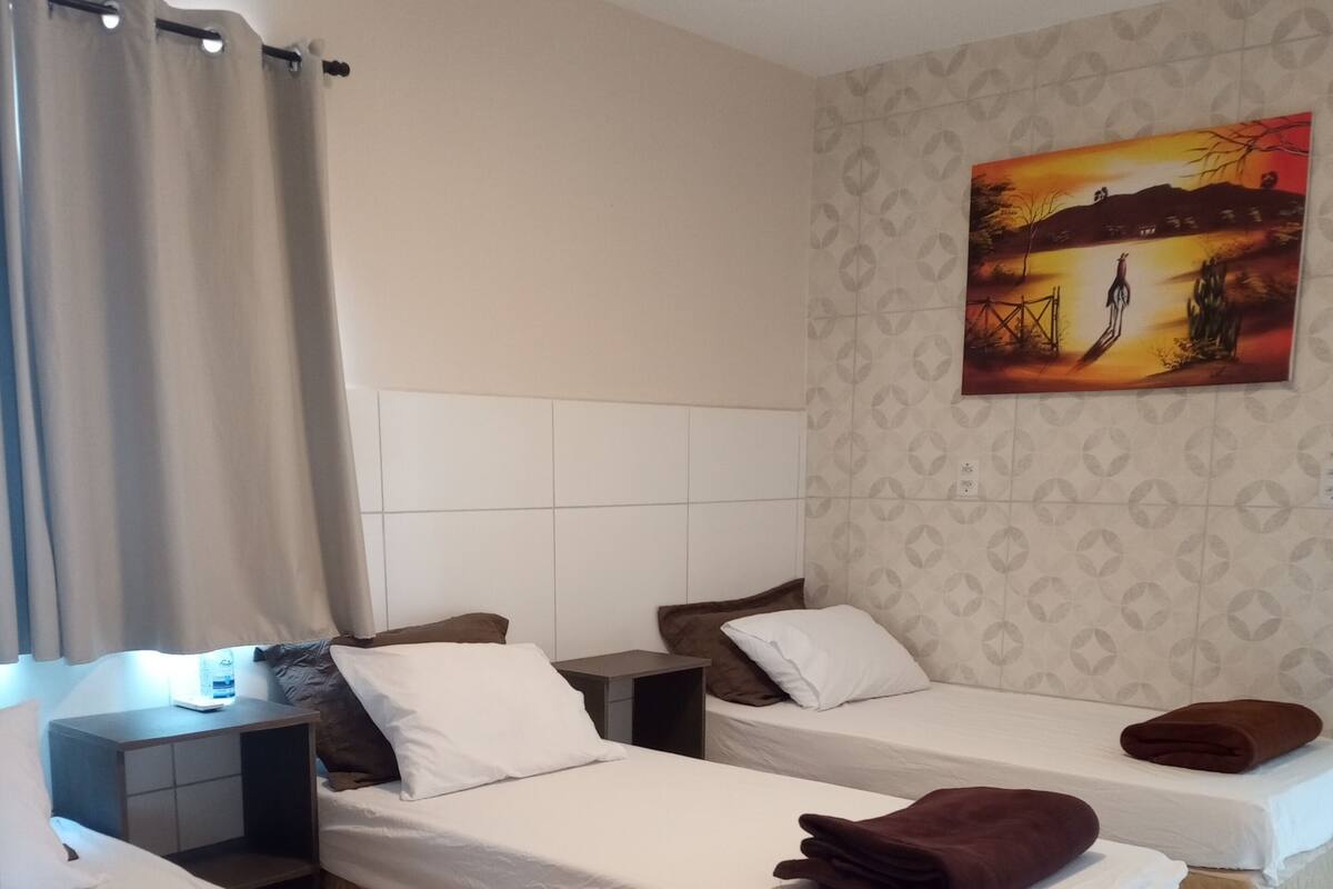 A hotel room with three beds, a headboard, a painting on the wall, and a curtain.