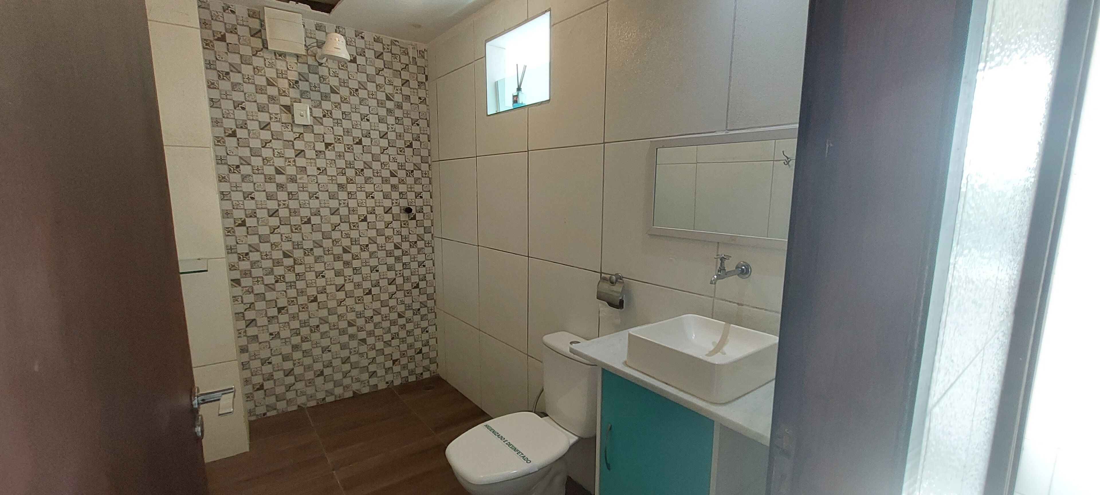 Een badkamer met een betegelde muur, toilet, wastafel en spiegel.