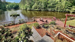 Una terraza con mobiliario exterior que da a un lago, rodeada de un área boscosa.