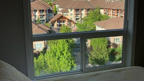 Ein Zimmer mit großem Fenster und Blick auf eine Wohngegend mit mehreren Gebäuden und einem Berg im Hintergrund.