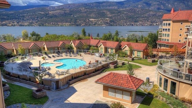 Ein Hotel mit Pool, Sitzgelegenheiten im Freien und Blick auf einen See und Berge.