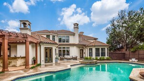 A residential property with a swimming pool, a covered patio, and a large house with multiple windows and a chimney. - Plano Mansion with Beautiful Pool (Plano)