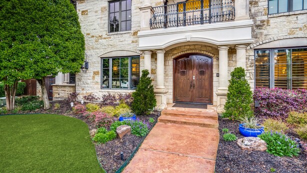 A two-story stone house with a front entrance, a balcony, and a well-maintained garden. - Plano Mansion with Beautiful Pool (Plano)