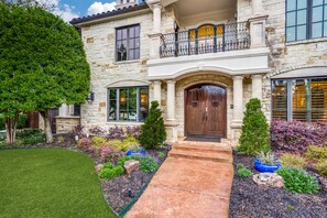 A two-story stone house with a front entrance, a balcony, and a well-maintained garden. - Plano Mansion with Beautiful Pool (Plano)